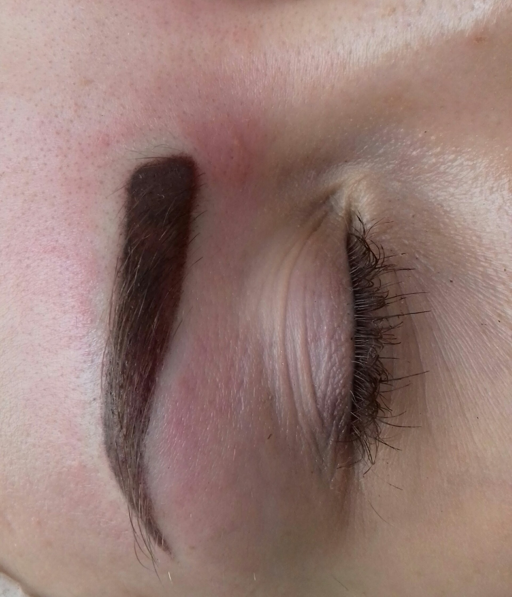 Zbliżenie na oko z widocznym brązem zabarwionym brwi permanentnej, skóra wokół oka lekko zaczerwieniona.