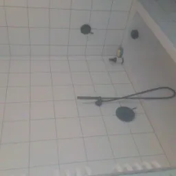 Białe płytki w łazience z czarną armaturą, widoczna bateria prysznicowa, słuchawka prysznicowa, mydło i szampon w rogu wanny, w trakcie remontu.