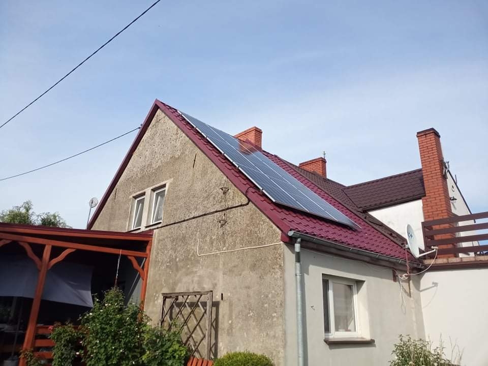 Dom jednorodzinny z panelami słonecznymi na czerwonym dachu, widoczne dwa kominy i antena satelitarna.