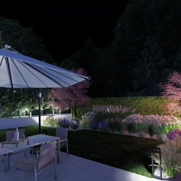 NIKO Biuro Architektury Krajobrazu - Oświetlony ogród nocą z parasolem nad stołem, różowe drzewo w tle. Nowoczesny design z lampami punktowymi i dekoracyjnymi trawami.