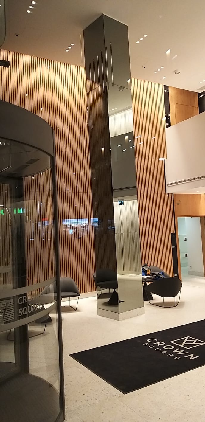 Wnętrze budynku z obrotowymi drzwiami, ścianą z drewnianych listew i lustrzaną kolumną.