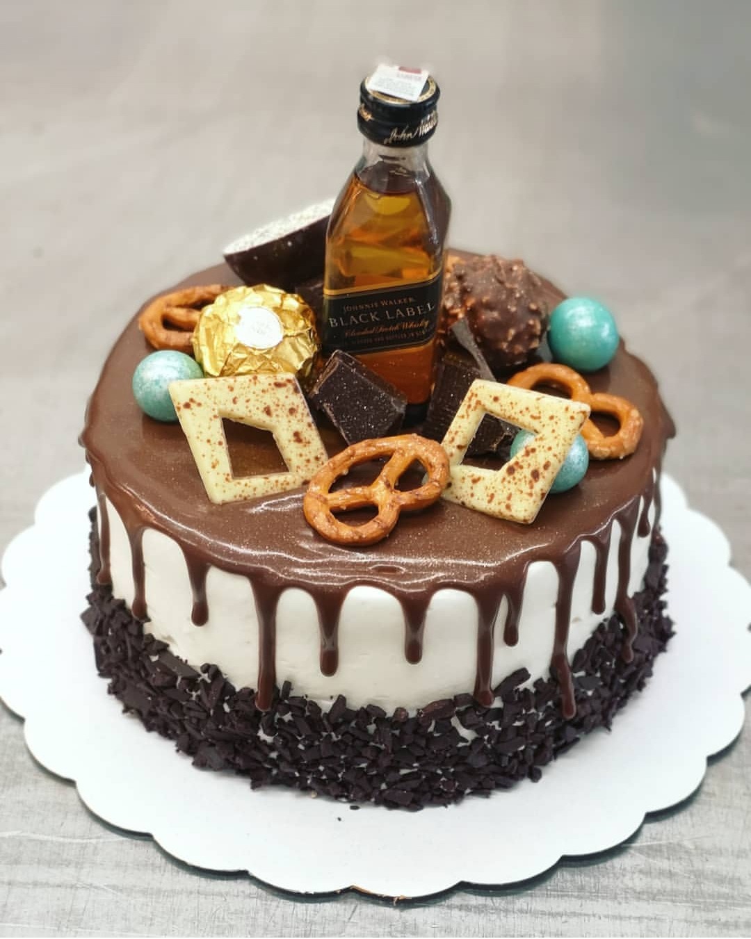 Tort z polewą czekoladową, ozdobiony miniaturową butelką whisky, pralinkami Ferrero Rocher, preclami i czekoladowymi dekoracjami.