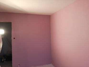 Pomalowane na różowo ściany w rogu pokoju, widoczny fragment otworu drzwiowego z niedokończonym wykończeniem.