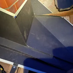 Szczegółowe ujęcie obróbki blacharskiej dachu z widocznymi elementami mocującymi i narzędziem dekarskim w trakcie montażu.