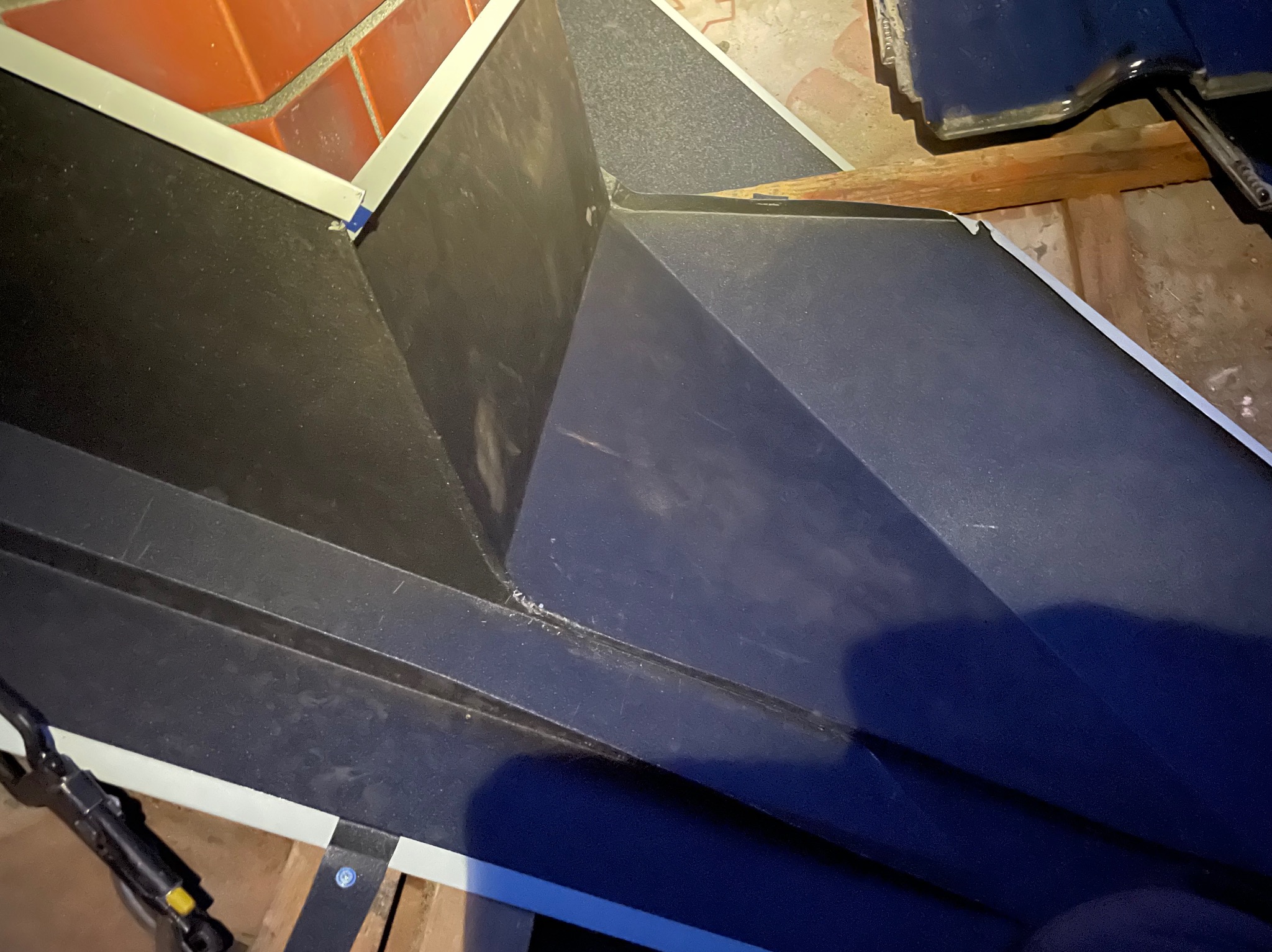 Szczegółowe ujęcie obróbki blacharskiej dachu z widocznymi elementami mocującymi i narzędziem dekarskim w trakcie montażu.