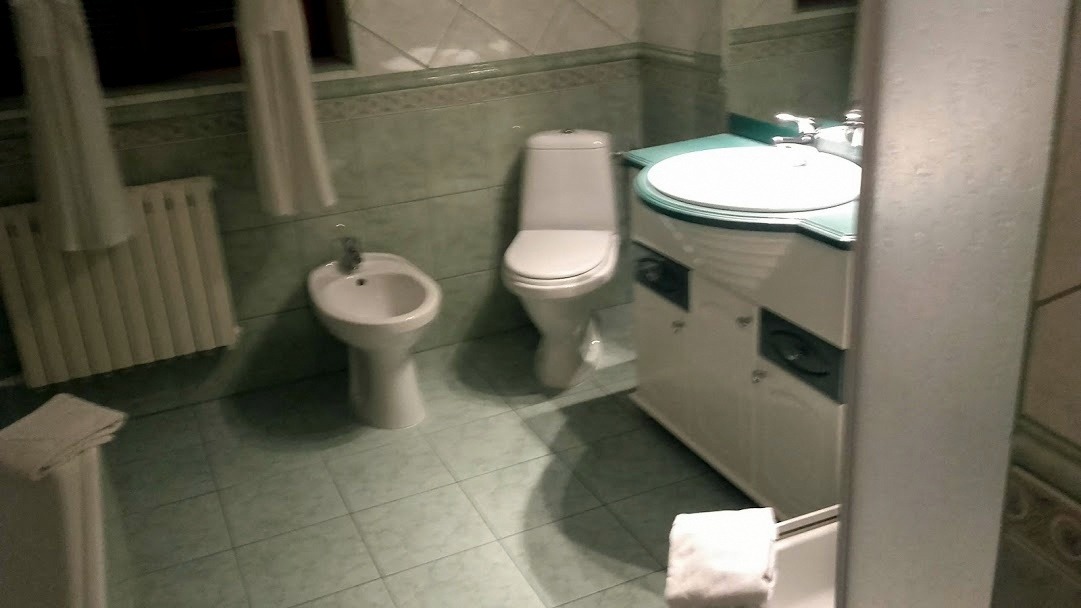 Łazienka z zielonymi płytkami, wyposażona w umywalkę z szafką, toaletę, bidet i grzejnik.