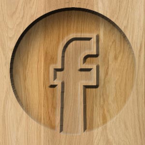 Wyżłobiony w drewnie okrągły znak 'f', przypominający logo Facebooka, z wyraźnym efektem cienia.