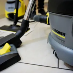 Profesjonalny odkurzacz Kärcher T 12/1, szaro-czarno-żółty, na jasnych płytkach podłogowych, widoczna ssawka i inne akcesoria w tle.