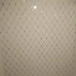 Ściana wyłożona białymi płytkami z szarym wzorem rombów i punktów w węzłach, odbicie światła na powierzchni płytek.