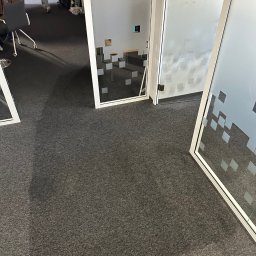 XCLEANERS - Szary dywan w biurze z trzema szklanymi ściankami działowymi z motywem kwadratów, widoczny fragment logotypu firmy na jednej z nich.