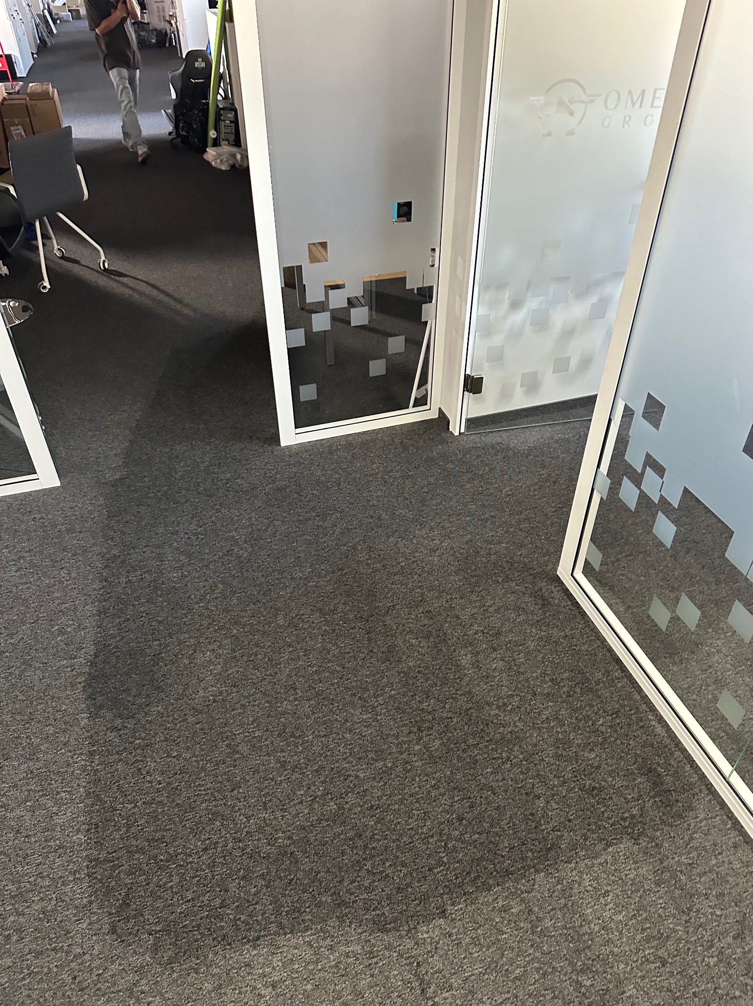 Szary dywan w biurze z trzema szklanymi ściankami działowymi z motywem kwadratów, widoczny fragment logotypu firmy na jednej z nich.