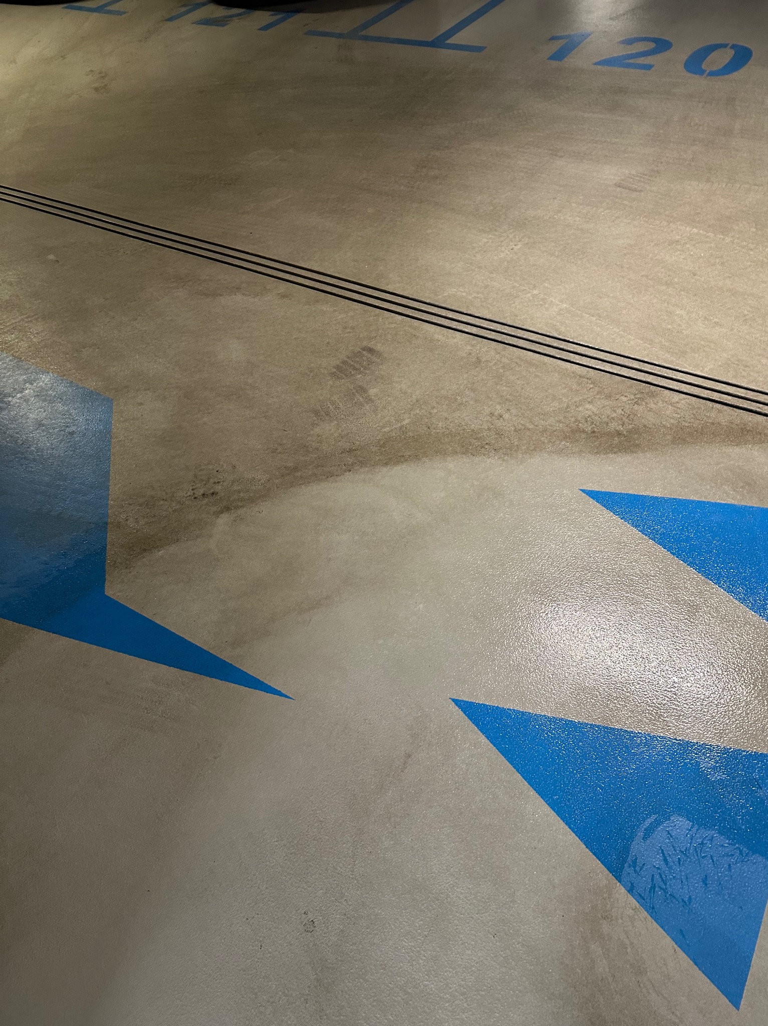 Fragment posadzki parkingowej z numerem '120' i niebieskimi elementami graficznymi, widoczny obszar po czyszczeniu, kontrastujący z zabrudzoną powierzchnią.