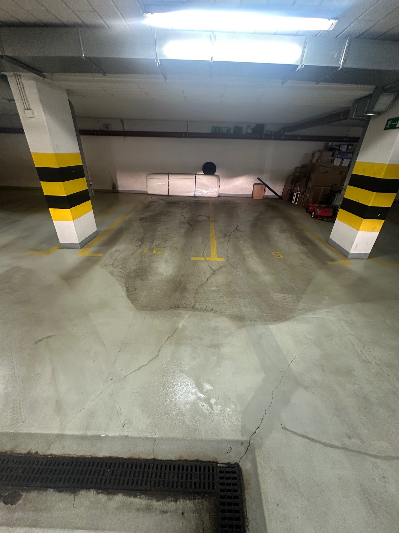Posadzka garażowa po czyszczeniu, widoczne ślady po oponach usunięte. Żółte linie wyznaczają miejsca parkingowe. Słupy z pasami ostrzegawczymi.