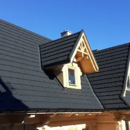 Czarny dach z blachodachówki na nowym drewnianym domu w stylu góralskim z oknami dachowymi, widok w słoneczny dzień.