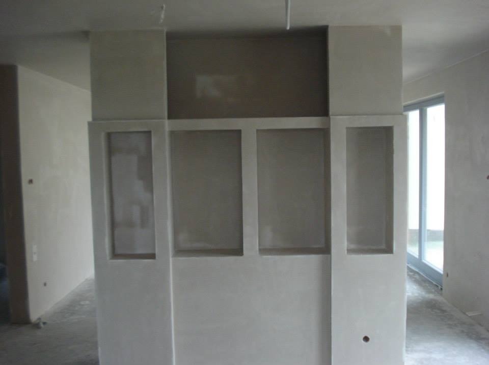 Świeżo otynkowana ściana z dekoracyjnymi wnękami w surowym, jasnym wnętrzu, widoczne ślady po pracach wykończeniowych na podłodze.