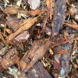 Mieszanka kory drzewnej o różnej fakturze i odcieniach brązu, z widocznymi fragmentami drewna i igliwia, układająca się w naturalną kompozycję.