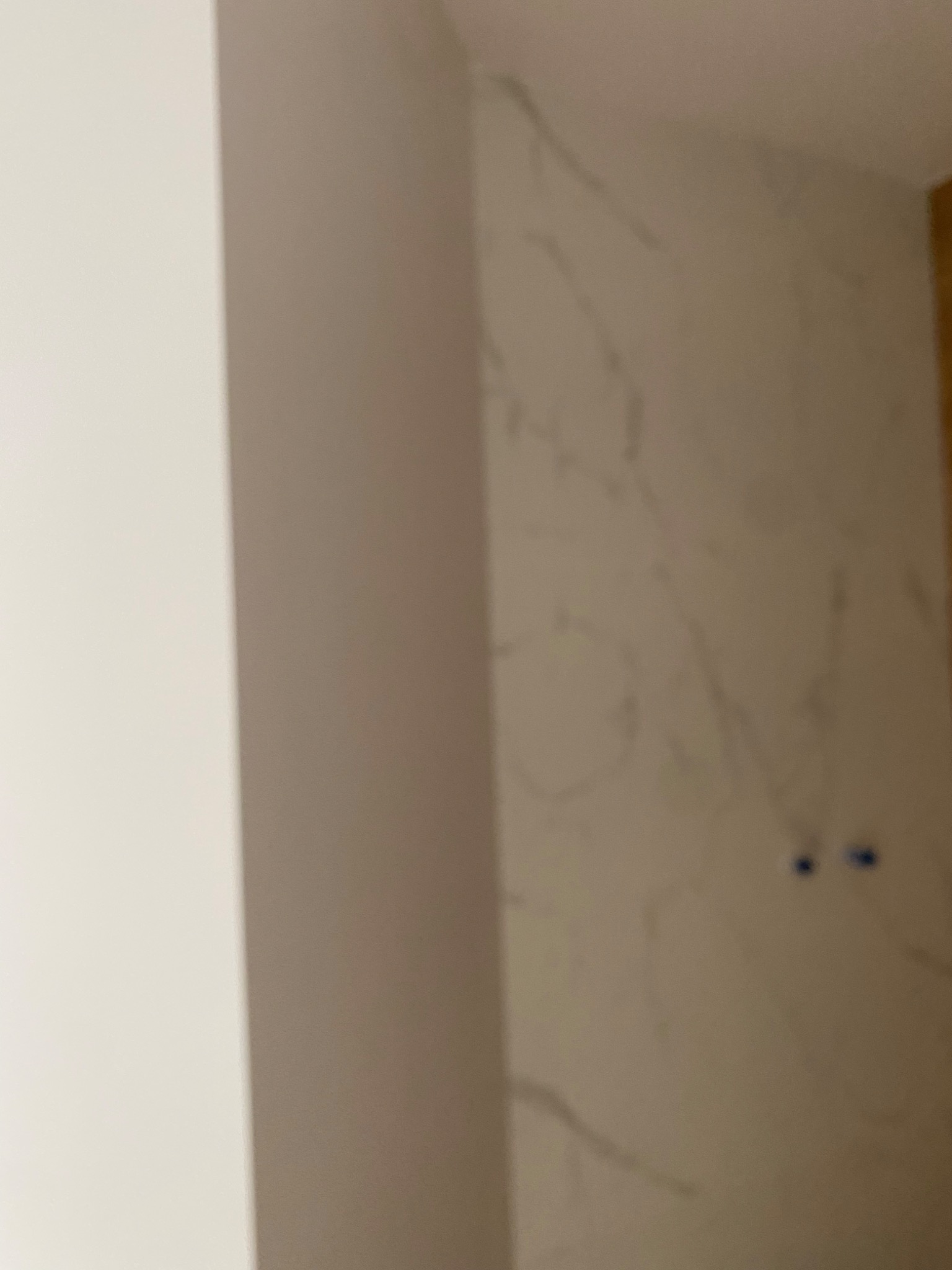 Fragment ściany z efektem marmuru, widoczne dwa otwory na gniazdka elektryczne przed malowaniem, z lewej strony widoczny fragment narożnika.