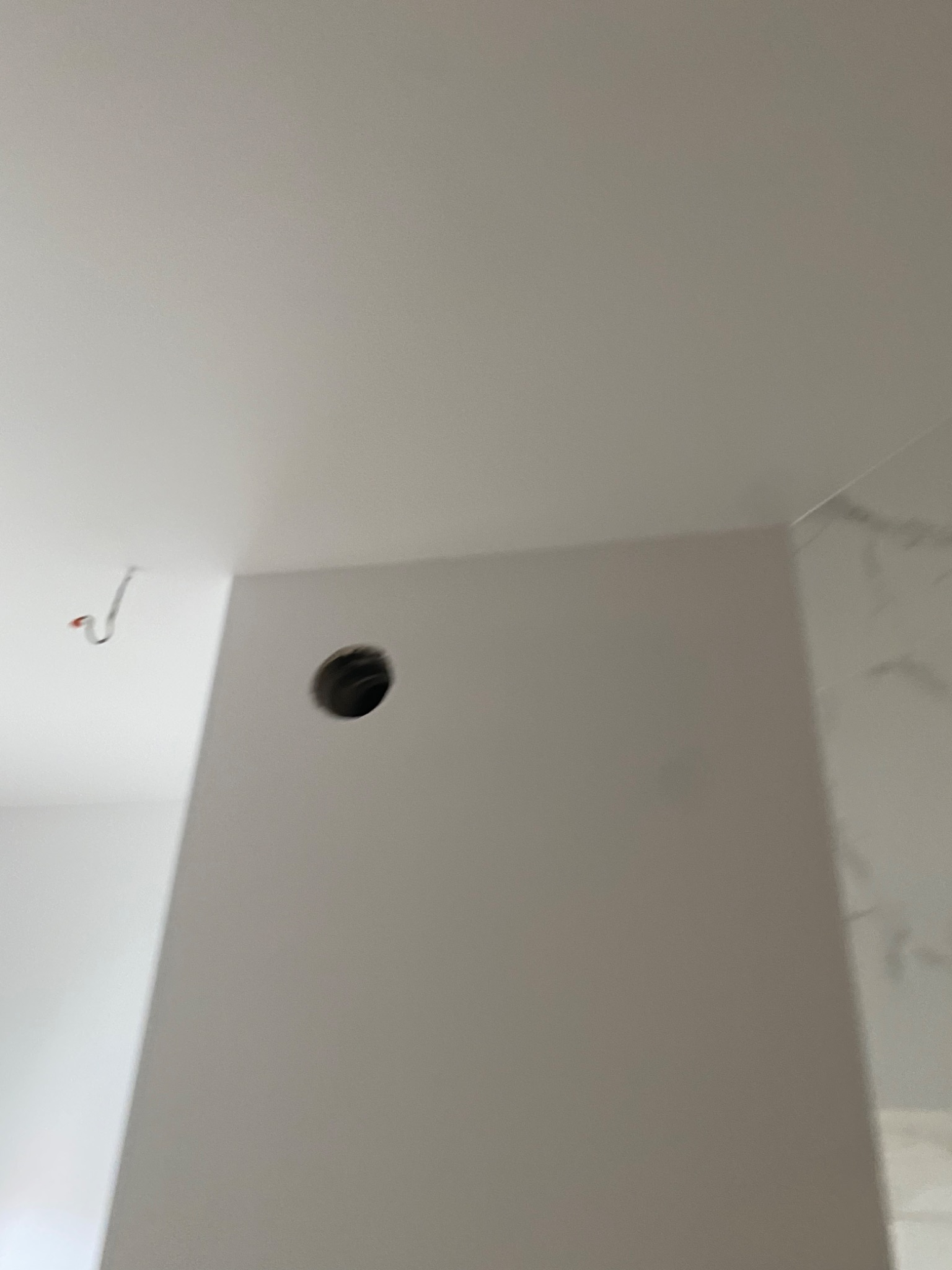 Świeżo pomalowana ściana z wywierconym otworem na instalację elektryczną i wystającym kablem z sufitu, widoczny fragment marmurowej płytki.