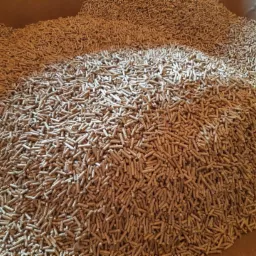 Ogromny stos jasnobrązowego pelletu drzewnego w magazynie, wypełniający kadr od dołu do góry.