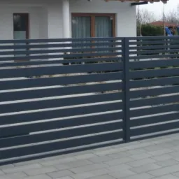 Nowoczesna, pozioma brama panelowa w kolorze grafitowym z automatyką, uzupełniająca ogrodzenie posesji z kostki brukowej.