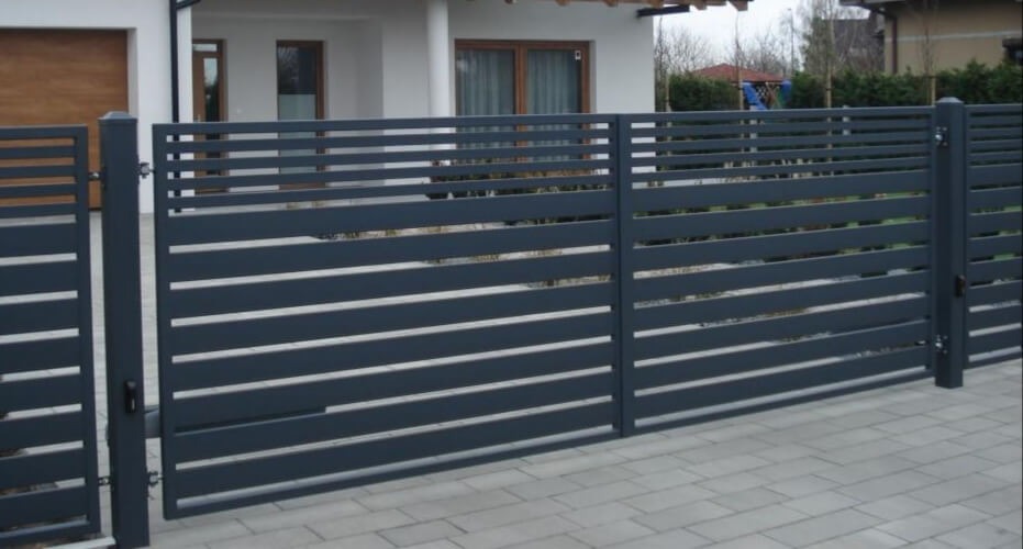 Nowoczesna, pozioma brama panelowa w kolorze grafitowym z automatyką, uzupełniająca ogrodzenie posesji z kostki brukowej.