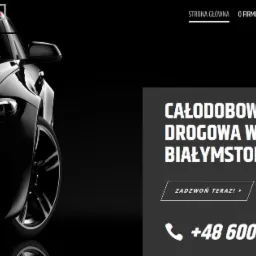 Częściowy widok czarnego samochodu z charakterystycznymi, okrągłymi światłami LED, z logo 'MOTOFIRMA Andrysewicz' w lewym górnym rogu oraz informacją o całodobowej pomocy drogowej w Białymstoku po...