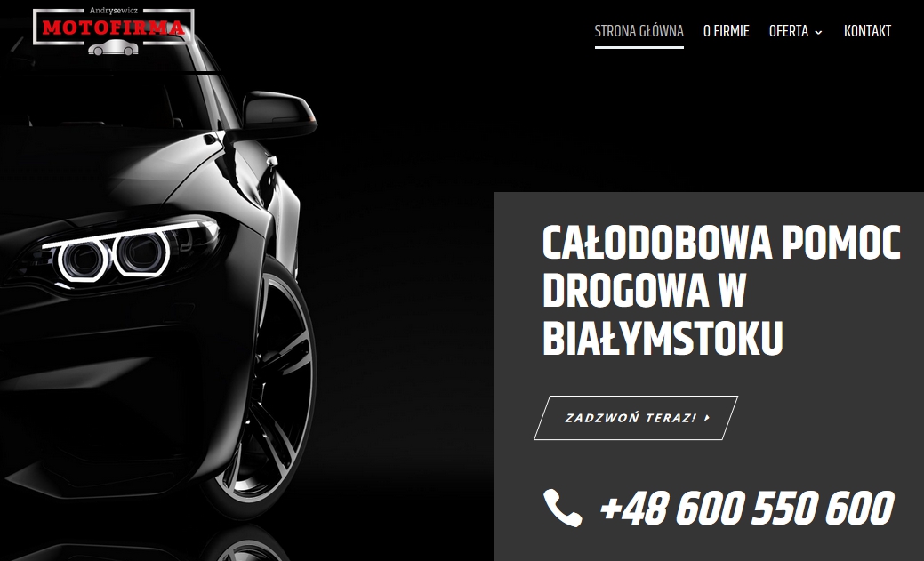 Częściowy widok czarnego samochodu z charakterystycznymi, okrągłymi światłami LED, z logo 'MOTOFIRMA Andrysewicz' w lewym górnym rogu oraz informacją o całodobowej pomocy drogowej w Białymstoku po...