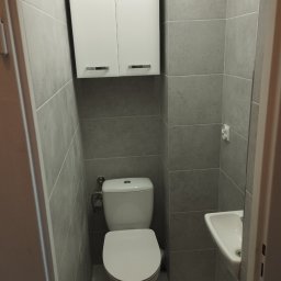 Katarzyna Grzesiek Fragles Usługi remontowo budowalne - Nowoczesna, mała łazienka w szarościach z podwieszaną toaletą i szafką nad nią, oraz małą umywalką narożną.