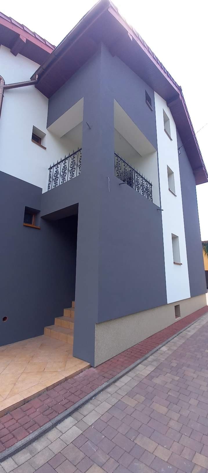 Dwukondygnacyjny budynek po remoncie elewacji, z szarą i białą kolorystyką, balkonem z ozdobną balustradą i wykończonym wejściem z brązowymi płytkami.