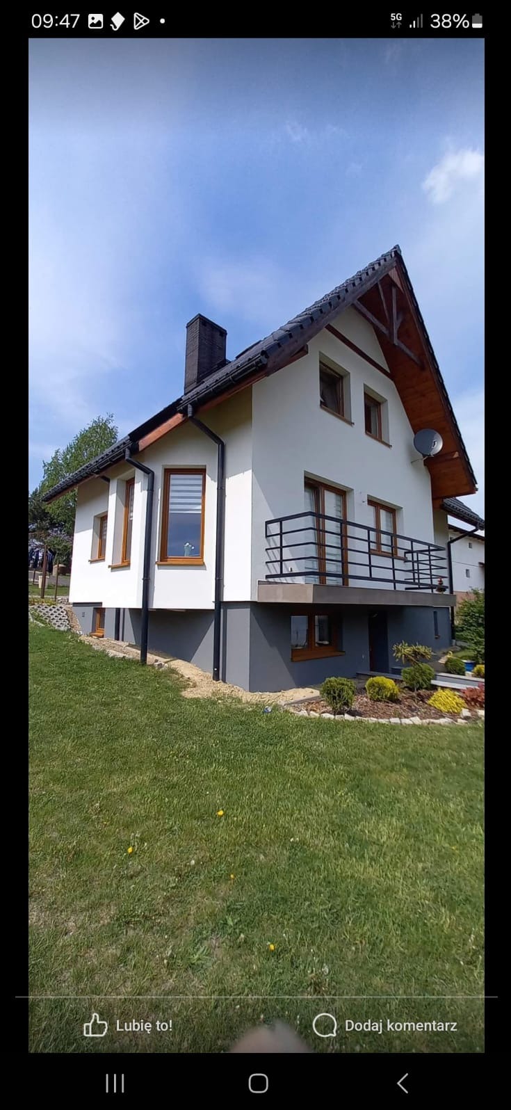 Dwukondygnacyjny dom jednorodzinny z balkonem, po renowacji elewacji, z nowymi oknami w drewnianych ramach i pomalowaną na szaro podmurówką, na tle zielonego trawnika.