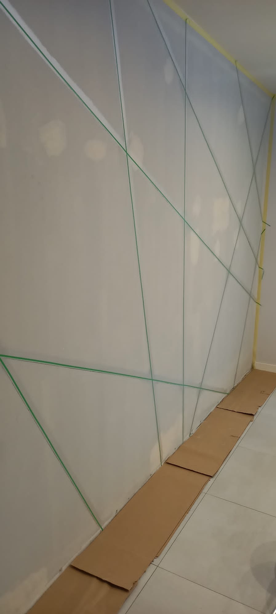 Przygotowana ściana do malowania z użyciem folii ochronnej i taśmy malarskiej, podłoga zabezpieczona kartonem.