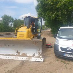 P.P.H.U. SYSTEM - Żółty spychacz Komatsu z brudnym lemieszem stoi obok białego busa z logo firmy System na tle torów kolejowych i drzew