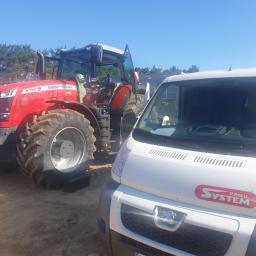 P.P.H.U. SYSTEM - Czerwony ciągnik rolniczy Massey Ferguson 8730S z otwartymi drzwiami kabiny, zaparkowany obok białego samochodu dostawczego z logo firmy SYSTEM P.P.H.U. na tle piaszczystego terenu i błękitnego nieba.