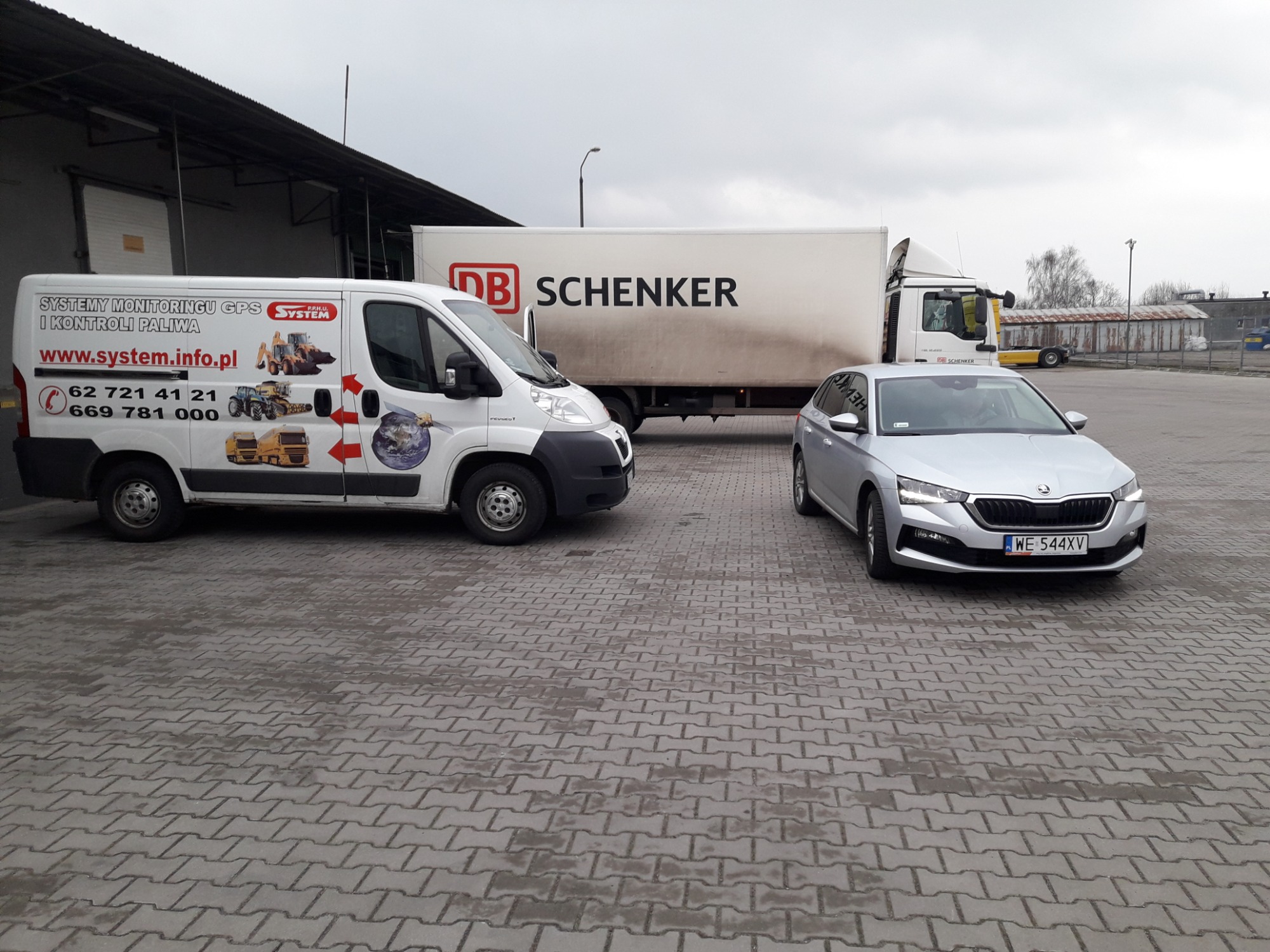 Flota pojazdów na szarym brukowanym placu: biała furgonetka z grafiką systemów monitoringu GPS i kontroli paliwa, ciężarówka DB Schenker i srebrna Skoda z tablicą rejestracyjną WE 544XV.