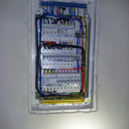 Rozdzielnica elektryczna z zainstalowanymi bezpiecznikami i okablowaniem, umieszczona w ścianie na tle surowego tynku.