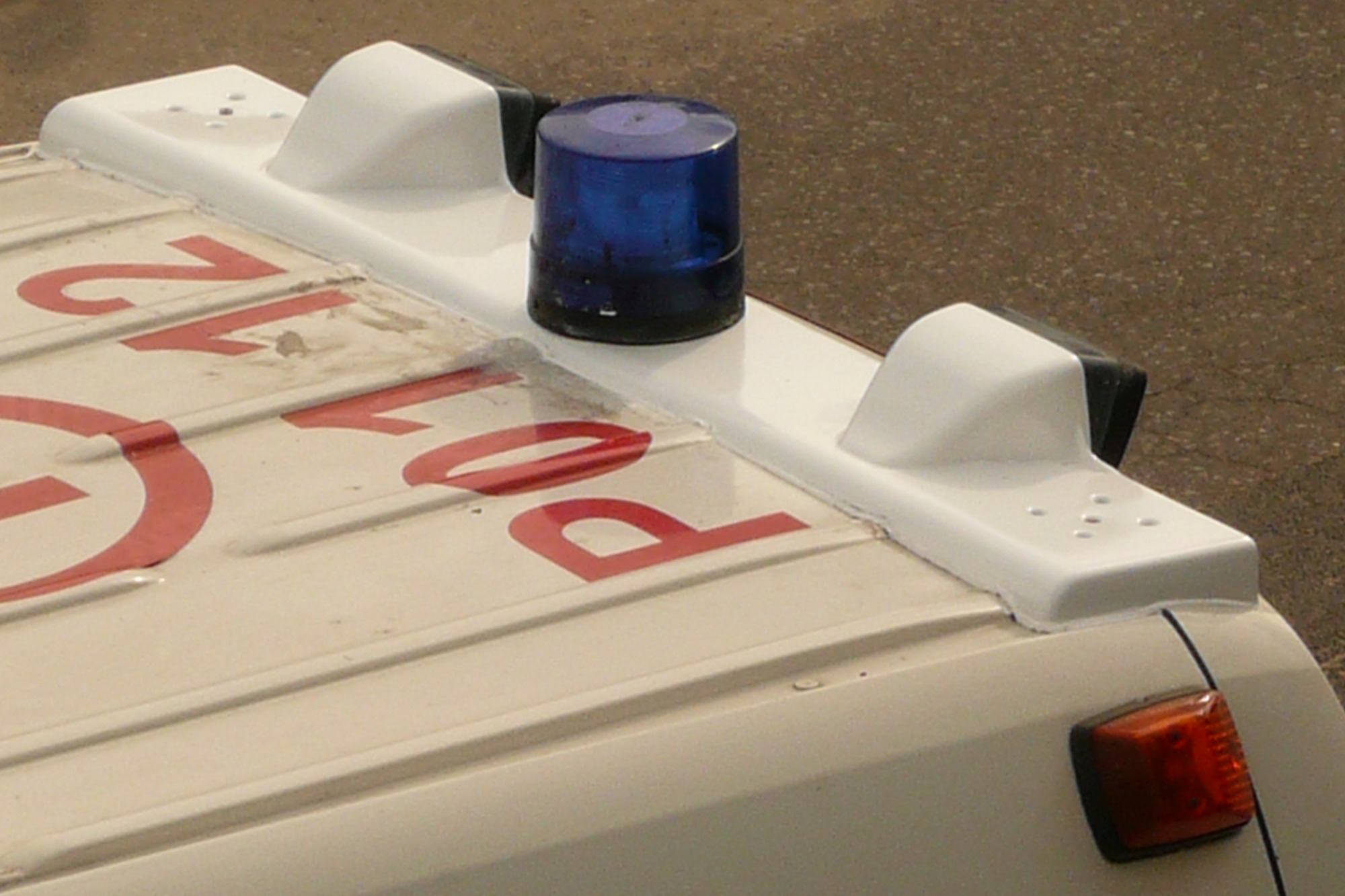 Fragment dachu pojazdu z napisem 'Pol 12', niebieskim kogutem i białymi elementami aerodynamicznymi.