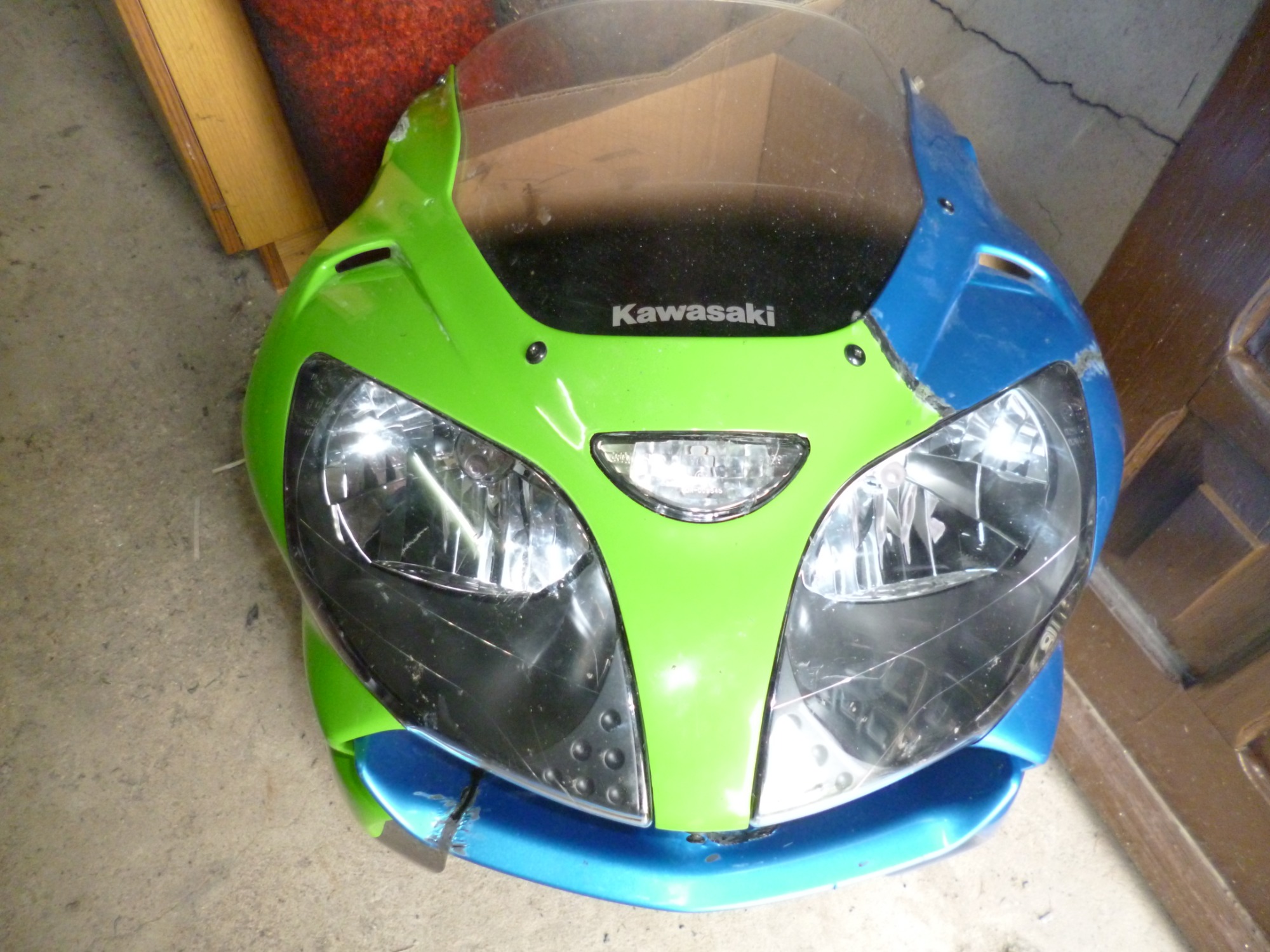 Przedni owiewka motocykla Kawasaki, pomalowana na zielono i niebiesko, z widocznymi śladami użytkowania i drobnymi uszkodzeniami lakieru.