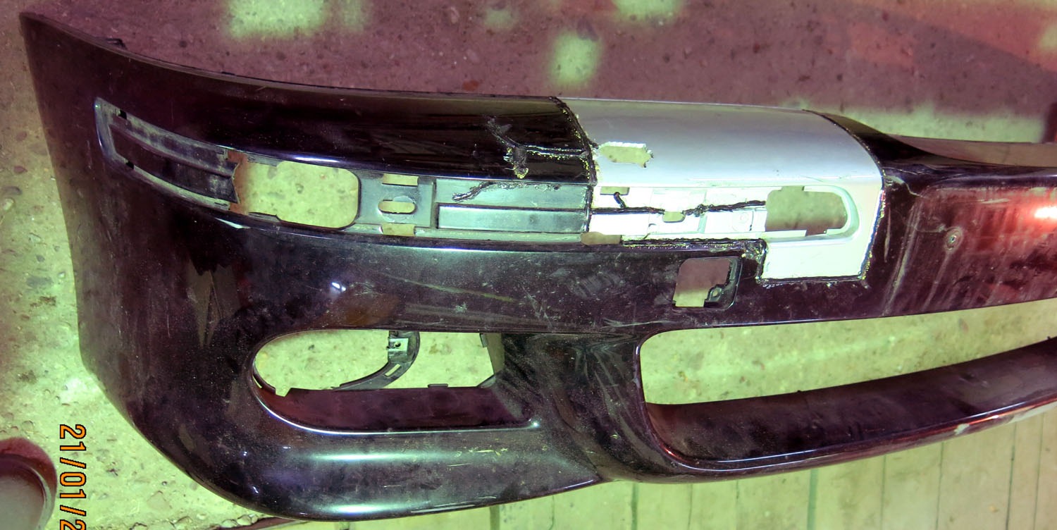 Uszkodzony, czarny zderzak samochodowy w trakcie naprawy, z widocznymi śladami szpachlowania i przygotowania do lakierowania.