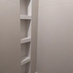 Wnęka z półkami w łazience, wyłożona jasnymi, matowymi płytkami ceramicznymi, widoczna krawędź wanny zabezpieczona folią.