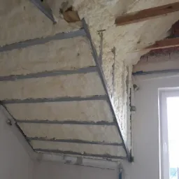 Poddasze w trakcie izolacji pianą PUR, widoczne profile metalowe konstrukcji pod płyty gipsowo-kartonowe i fragment okna.