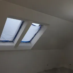 Świeżo pomalowane, białe poddasze w Rawie Mazowieckiej z oknami dachowymi zabezpieczonymi folią malarską, gotowe do dalszych prac wykończeniowych.