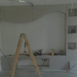 Łukasz - Ściana w trakcie wykańczania z dekoracyjnym łukiem i wnękami, widoczna drabina, narzędzia i laserowy poziom, surowy stan pomieszczenia.