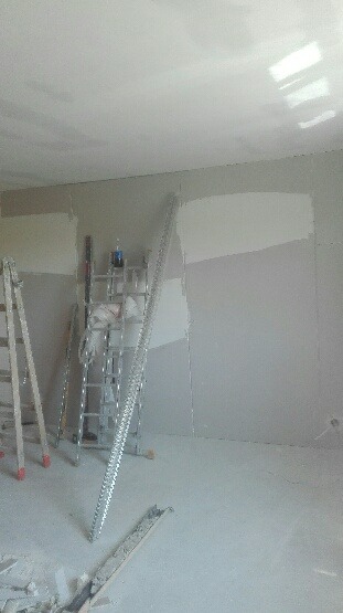 Pokój w trakcie remontu: ściany częściowo pokryte gładzią, drabiny i listwa przypodłogowa leżąca na podłodze.