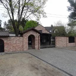 Nowoczesna posesja z ceglanym ogrodzeniem, metalową bramą wjazdową i brukowanym podjazdem. Brama dwuskrzydłowa z automatyką.