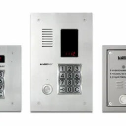 Trzy panele domofonowe z klawiaturą numeryczną, wykonane ze szczotkowanej stali, z wyświetlaczami LED prezentującymi numery, na białym tle.