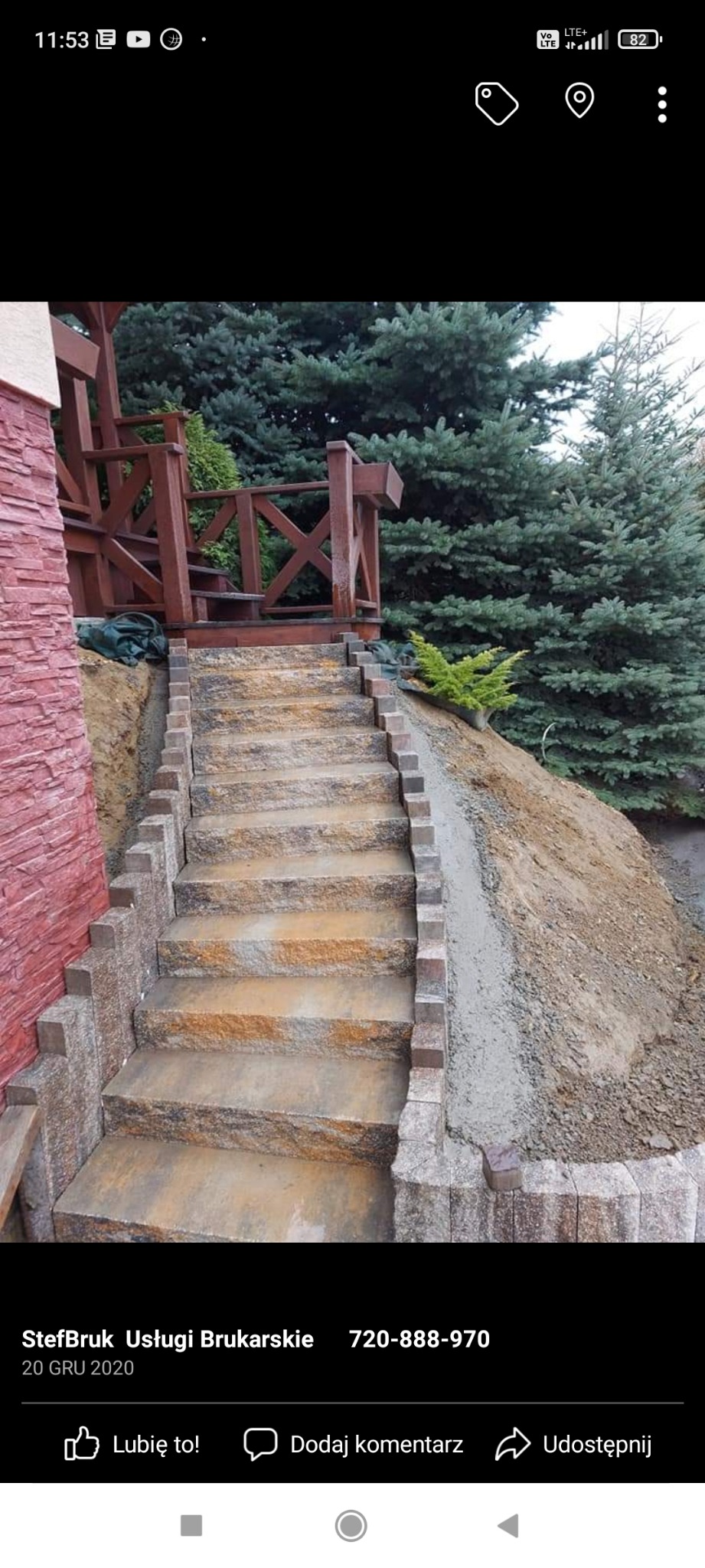 Schody zewnętrzne z kostki brukowej prowadzące do drewnianej konstrukcji, z widocznym obrzeżem i nasadzeniami roślinnymi w tle.