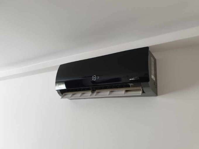 Czarna jednostka klimatyzacyjna typu split zamontowana na białej ścianie, wyświetlająca temperaturę 18 stopni Celsjusza.