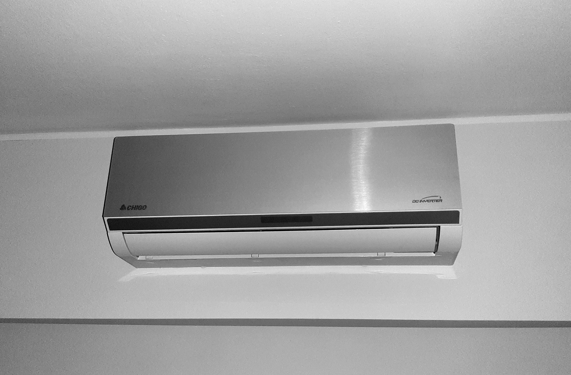 Zamontowany na ścianie, srebrny klimatyzator marki CHIGO z napisem DC Inverter, sfotografowany w czerni i bieli.