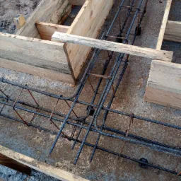 Zbrojenie w drewnianym szalunku przygotowane do zalania betonem, widok z góry na konstrukcję fundamentu.