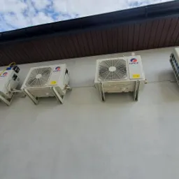 Szereg jednostek zewnętrznych klimatyzacji marki Gree zamontowanych na ścianie budynku, widoczna drabina i podłączone przewody serwisowe.